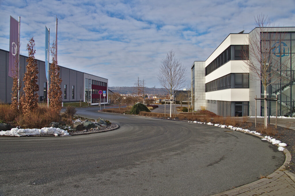 Aufnahme des Industriegebiets in Neu-Anspach. Neben einer sich windenden Straße sind moderne Gebäude zu sehen, die zur Firma Adam Hall gehören.